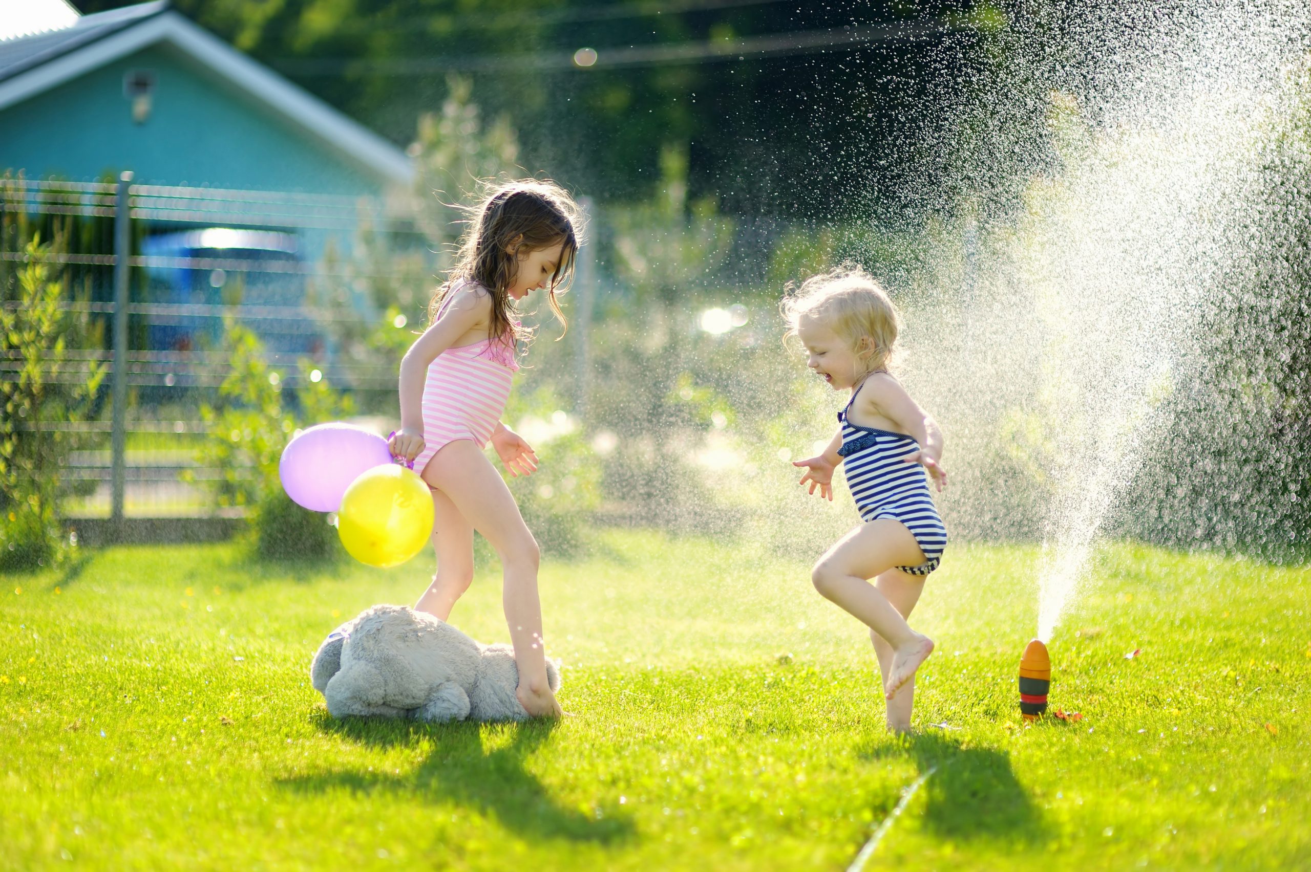 Little girls running though a sprinkler in a backyard